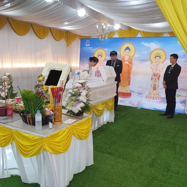Casket dressed with white chrysanthemums before a Buddha backdrop