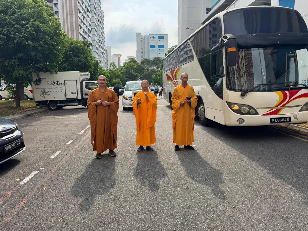 Monks leading the funeral procession, with the hearse and the coach waiting on the road